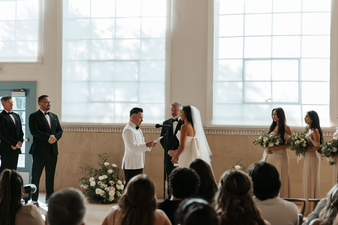 Groom reads handwritten vows to bride during indoor wedding ceremony.