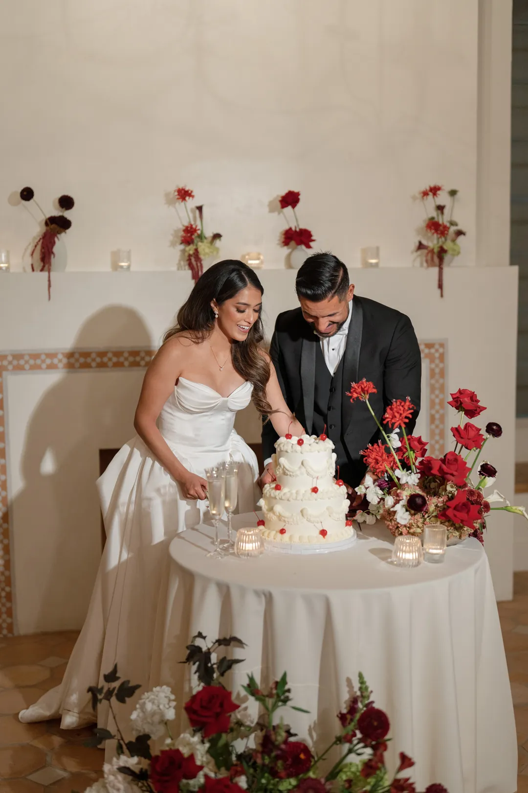 Bride and groom cut into 2-tiered vintage wedding cake with cherry details.