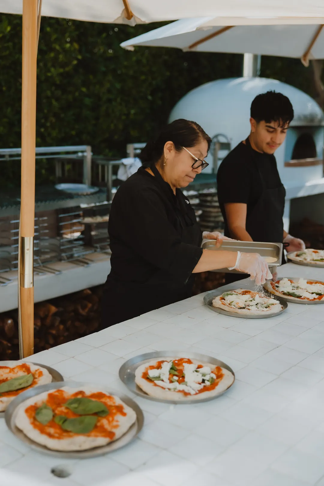 Chefs preparing pizzas at the outdoor kitchen counter