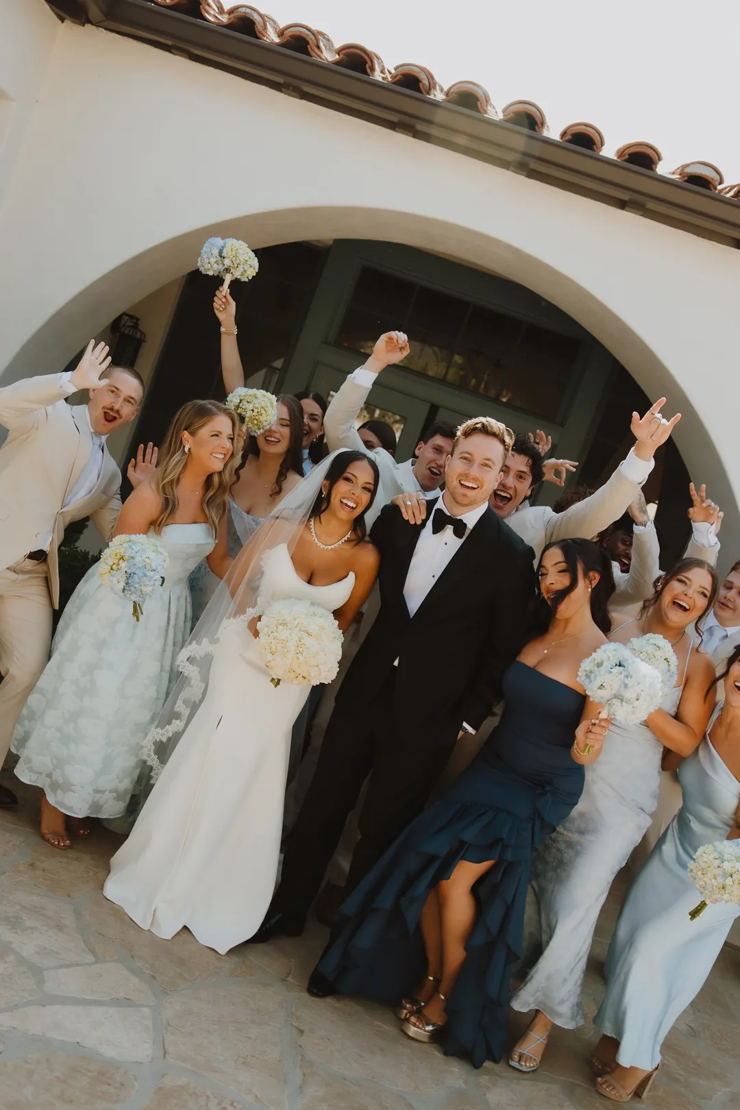 Wedding party celebrating together beneath an exterior archway.