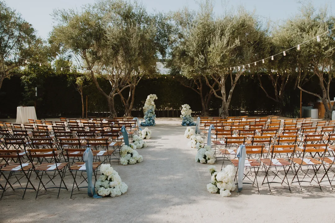 Ceremony aisle lined with white flowers beneath olive trees.