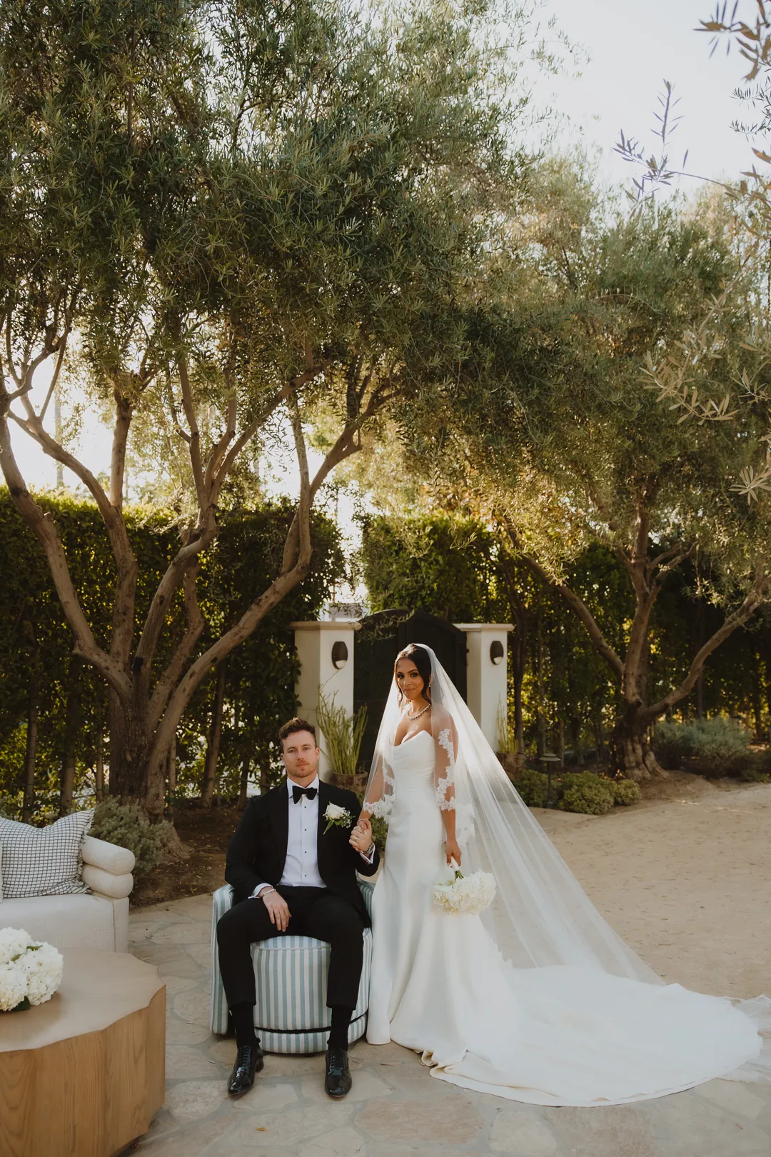 Bride standing beside the seated groom in the courtyard