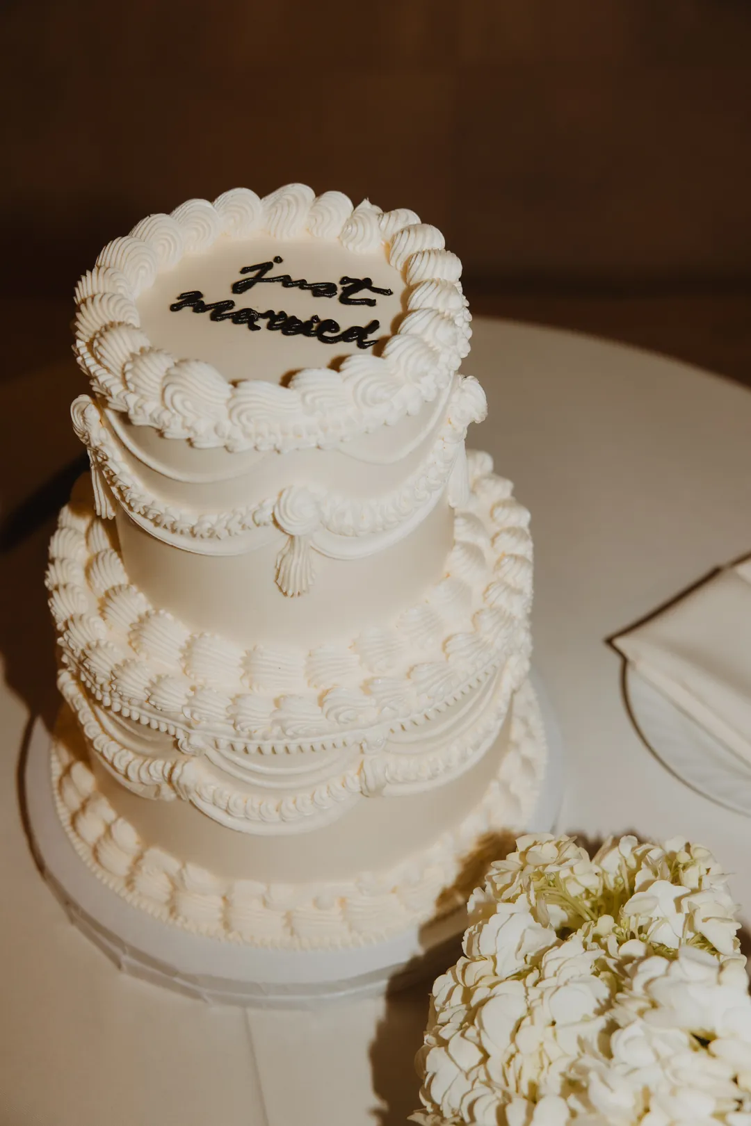 White tiered cake beside a floral arrangement