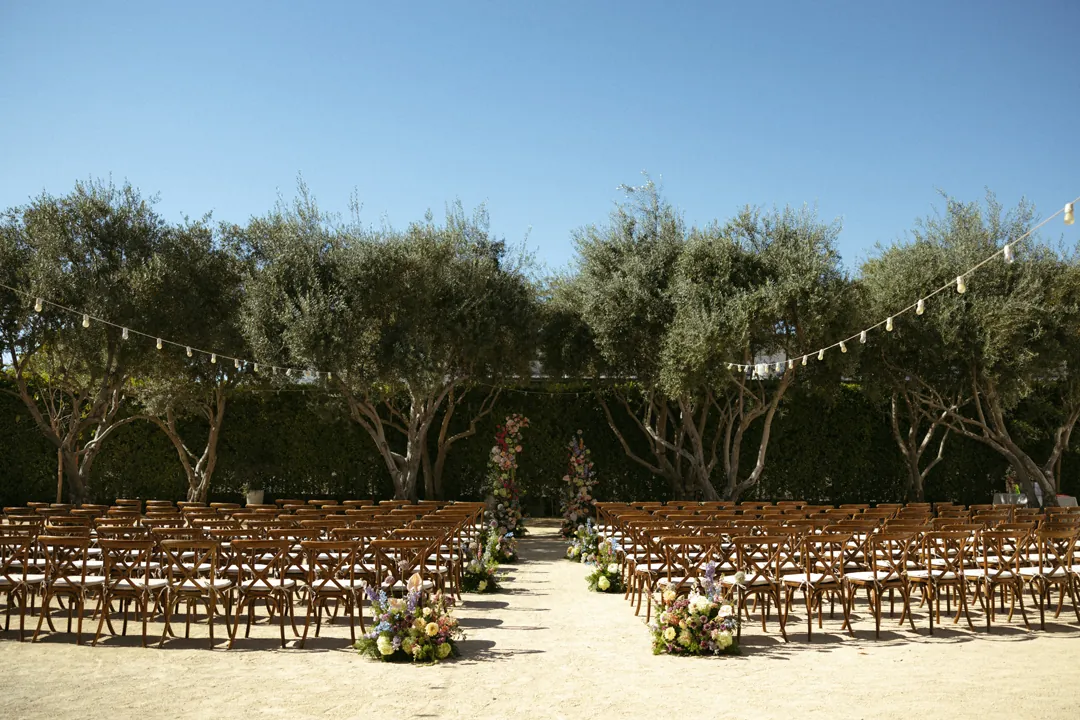 Outdoor ceremony chairs beside a flower-lined aisle