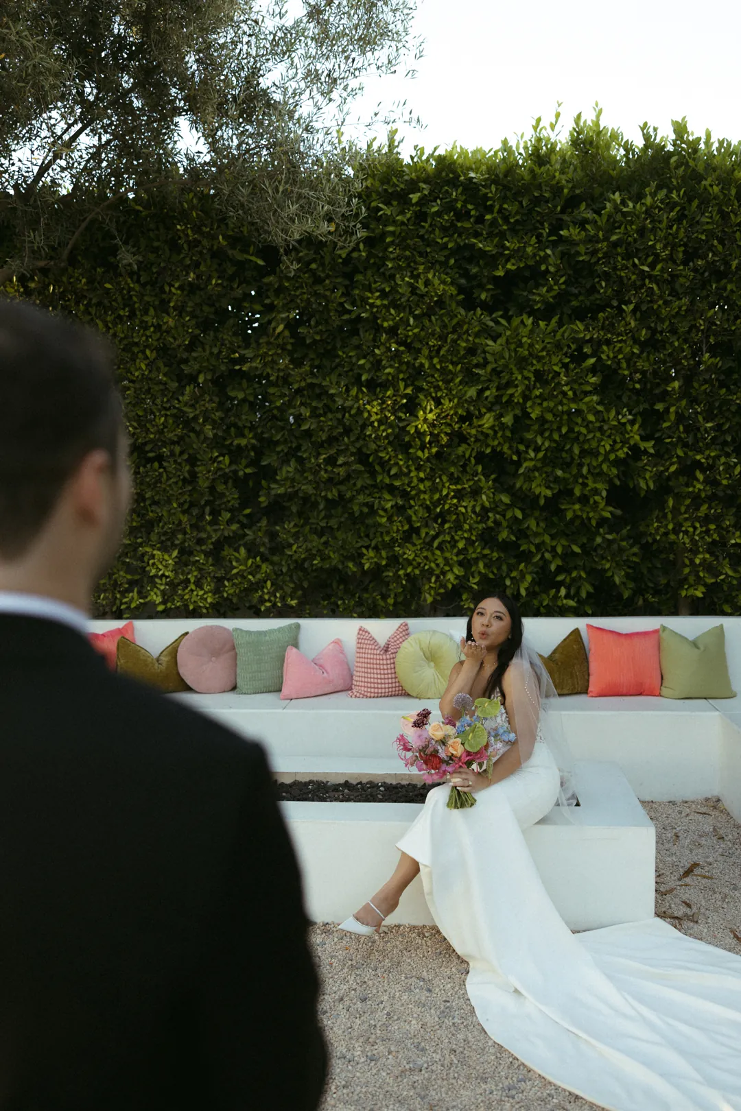 Bride seated beneath a hedge as the groom approaches