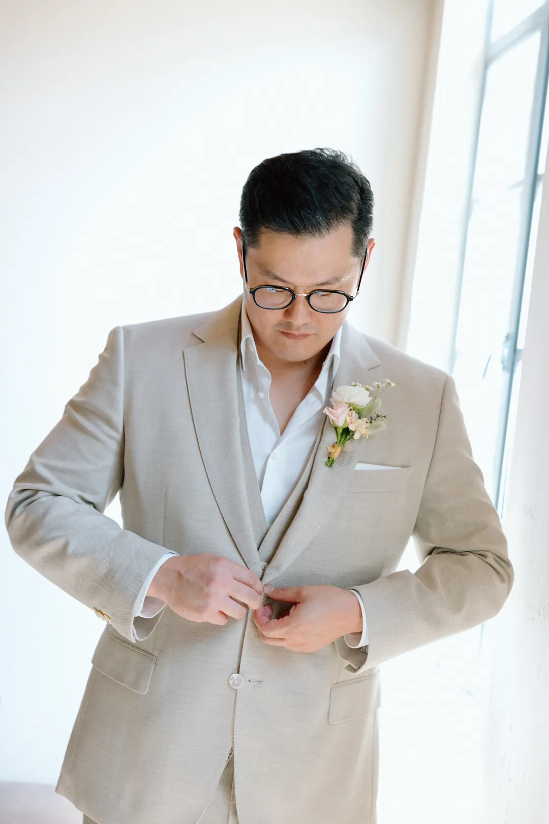 Groom fastening his light-colored suit jacket