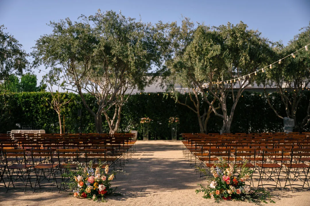 Empty outdoor ceremony aisle bordered by colorful flowers