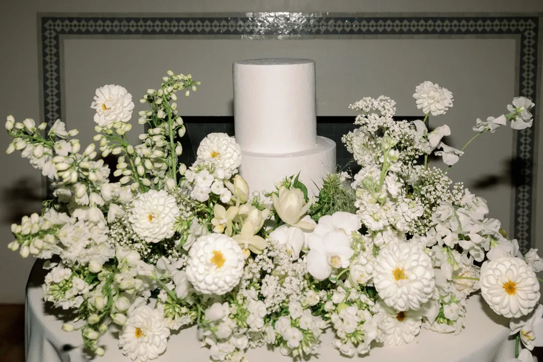 White tiered wedding cake surrounded by white flowers.