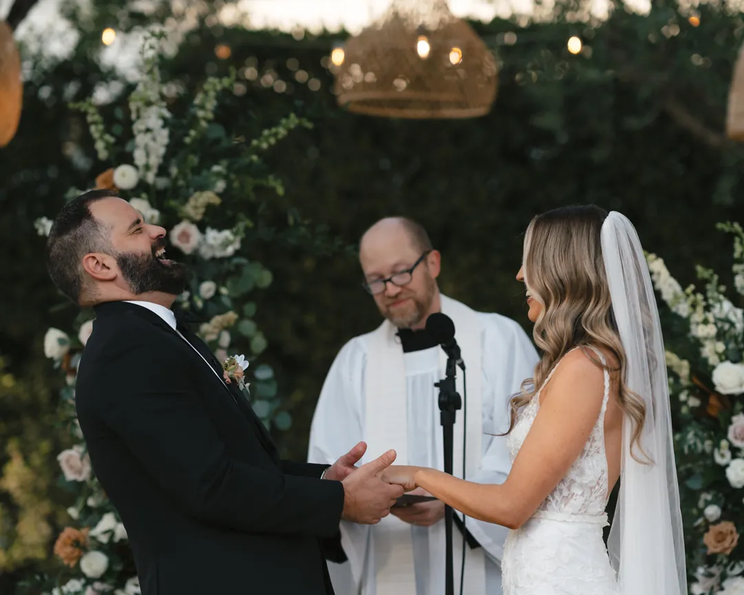 The couple holds hands while the officiant speaks at the outdoor ceremony.