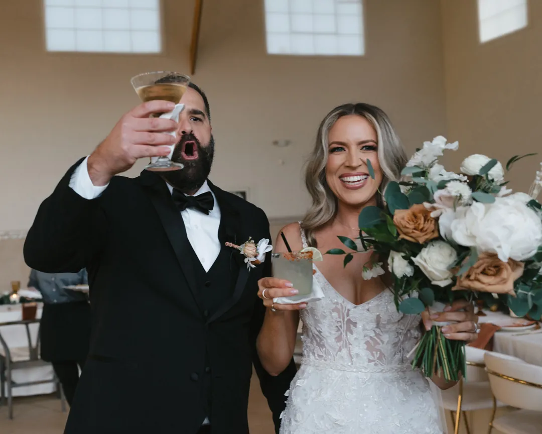 The couple raises drinks for a toast inside the reception hall.