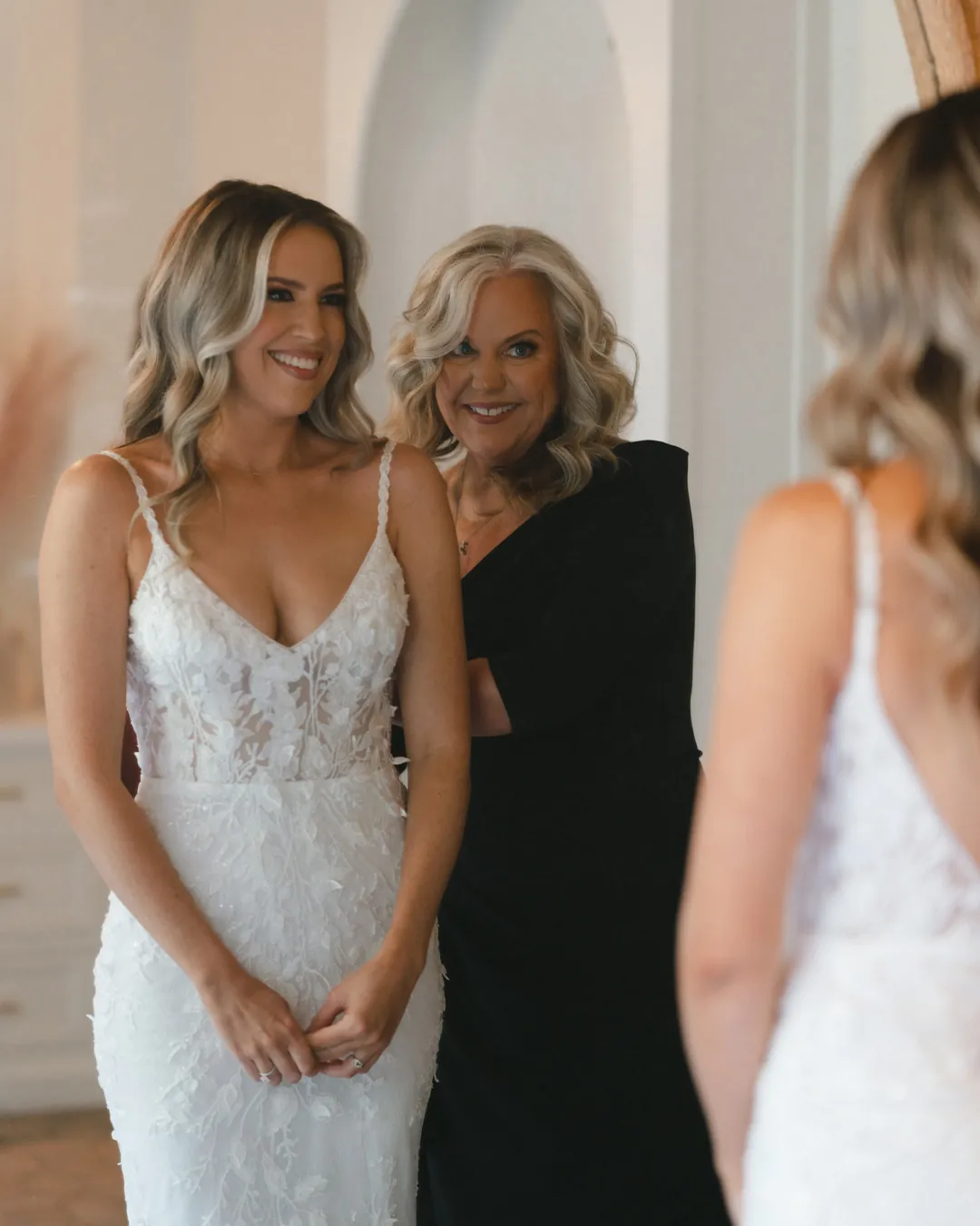 The bride smiles beside a helper in the dressing room.