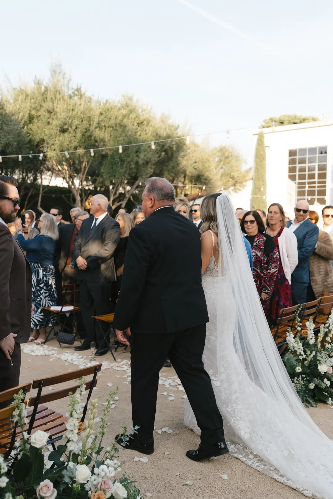 The bride walks down the outdoor ceremony aisle with an escort.