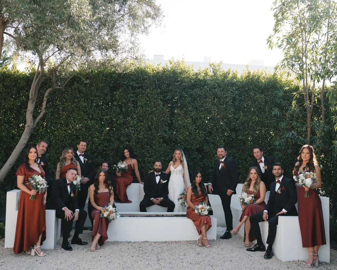 The wedding party poses around white outdoor lounge seating.