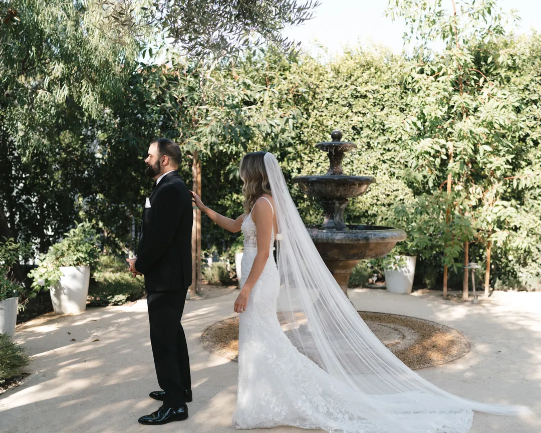 The bride approaches the groom beside a courtyard fountain.