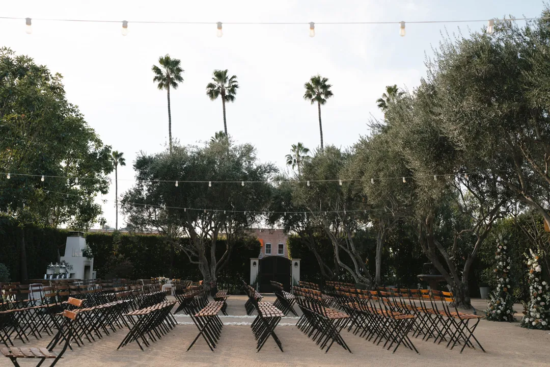 Ceremony chairs face the floral backdrop beneath olive trees.