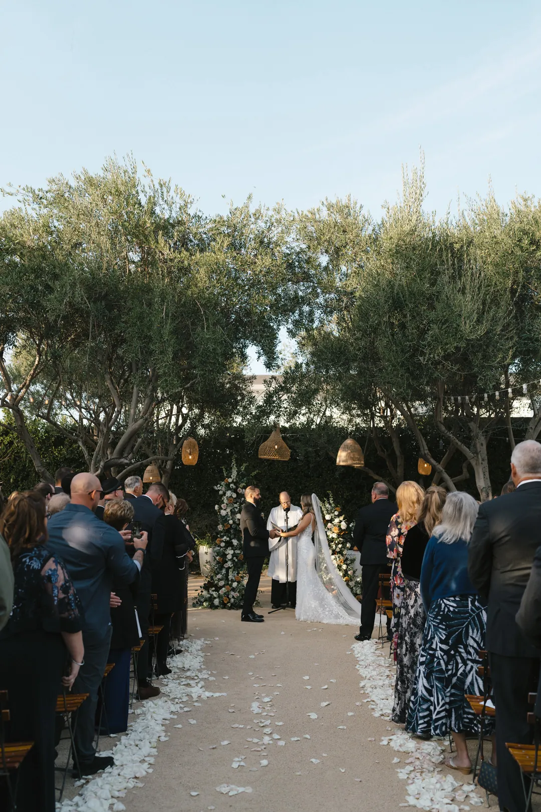 Standing guests line the petal-covered outdoor ceremony aisle.