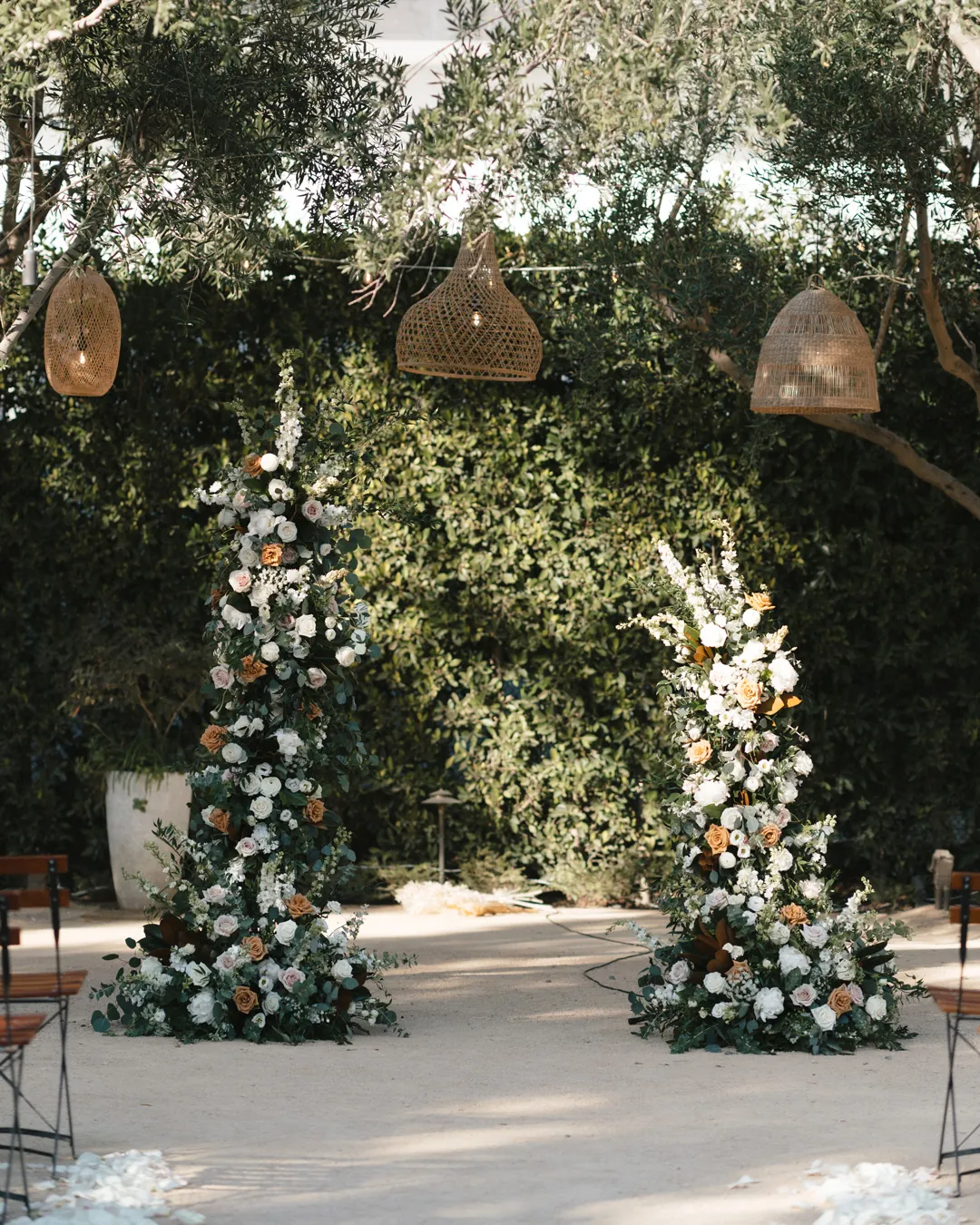 Tall floral arrangements frame a ceremony backdrop beneath hanging woven lights.