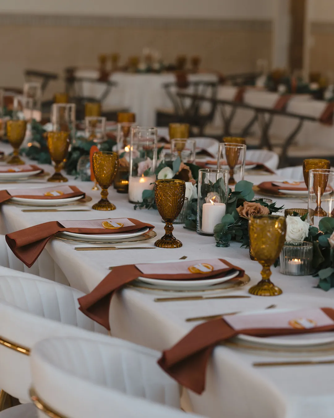 Reception place settings with amber glasses and terracotta napkins.