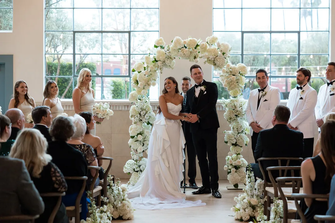 Bride and groom embracing beneath the white floral arch