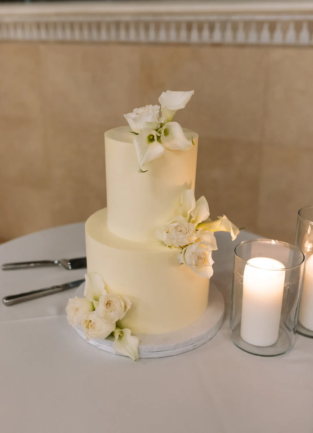 Two-tier white wedding cake with pale flowers and a candle