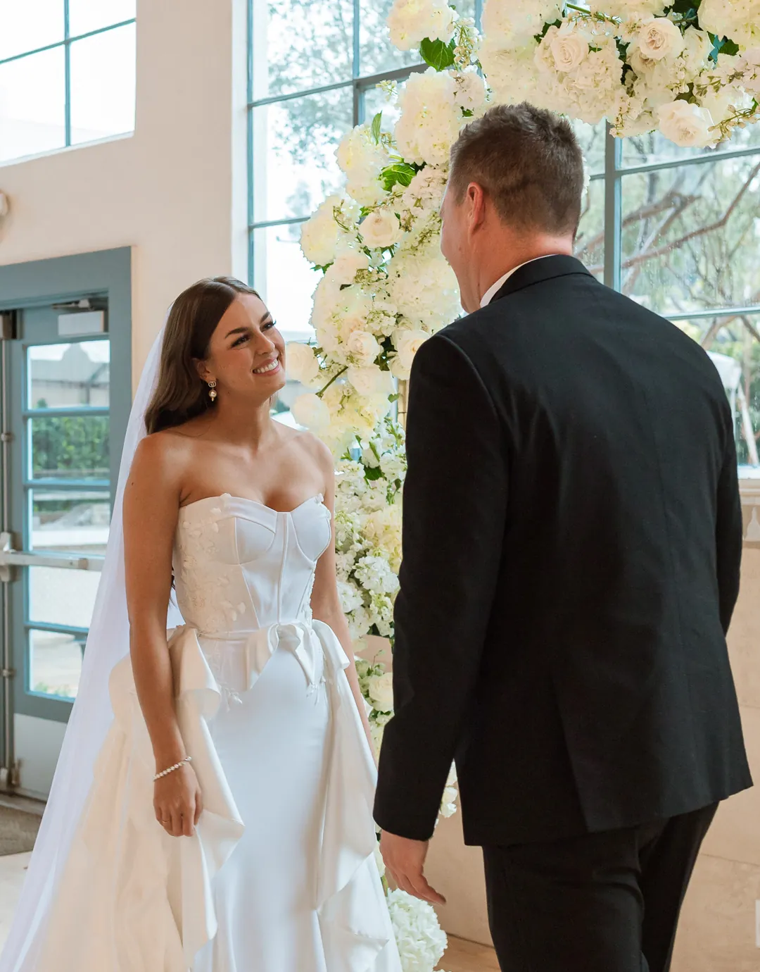 Bride smiling at the groom beneath the floral arch