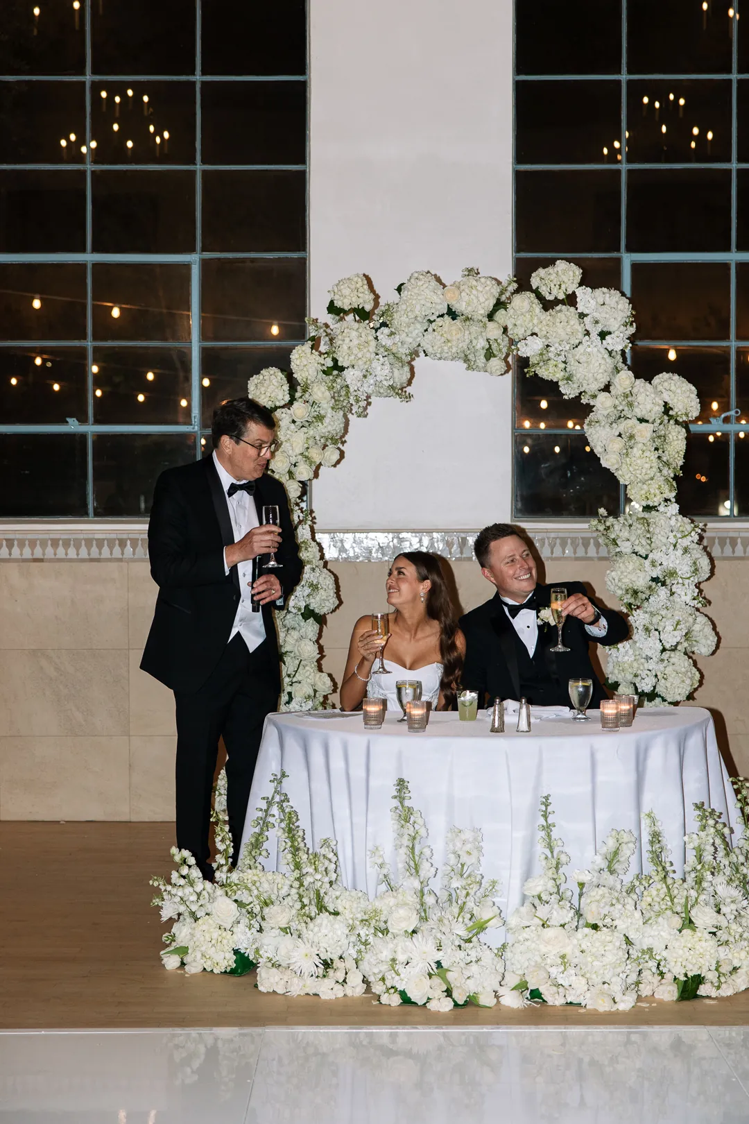 Guest giving a toast beside a flower-framed sweetheart table