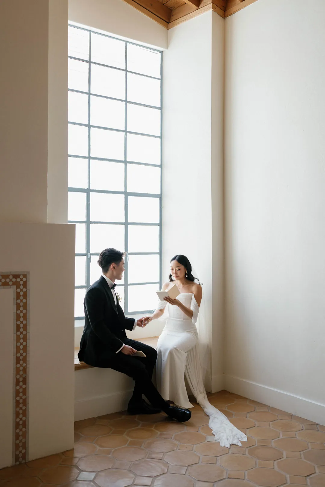 Bride and groom seated beside a tall window
