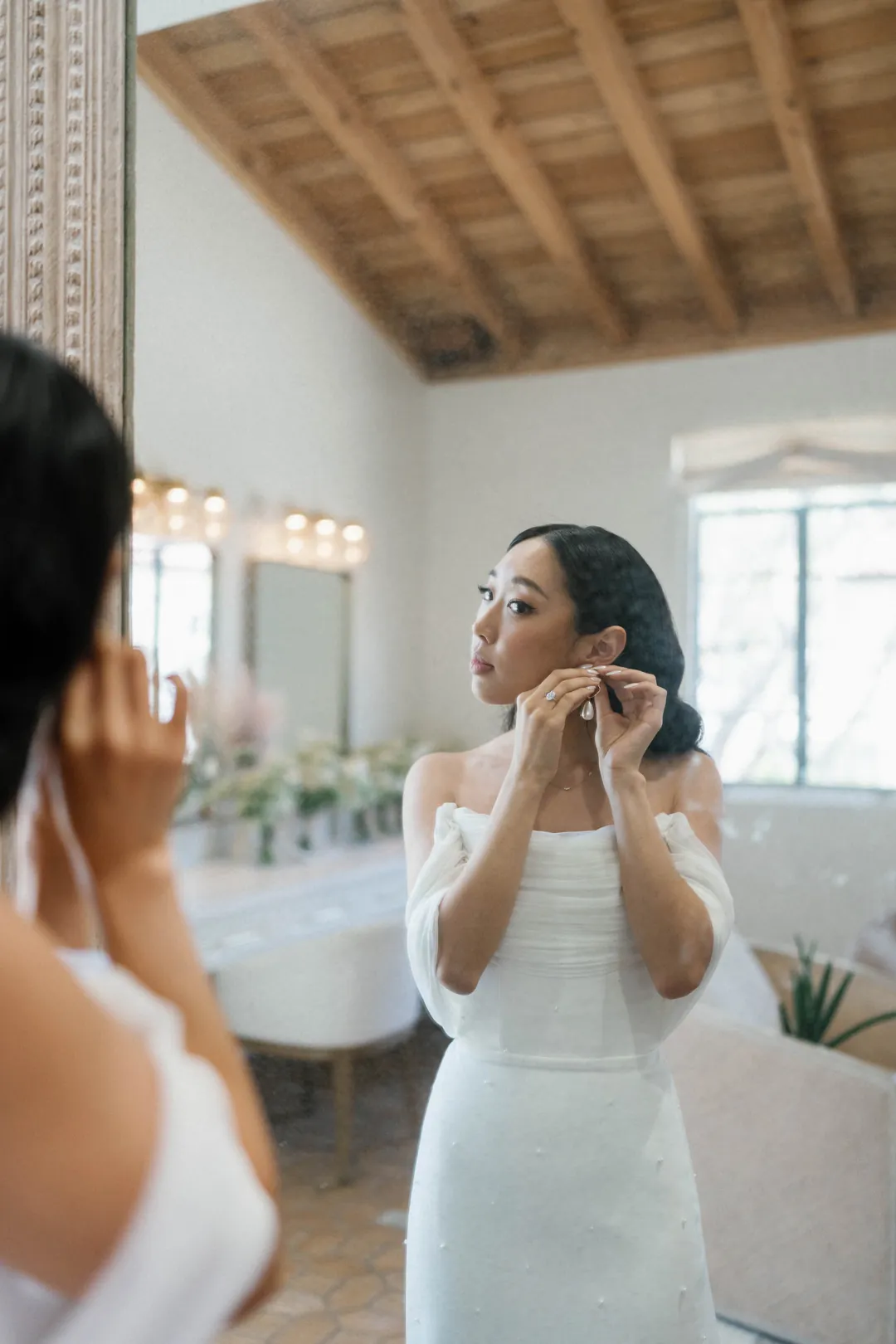 Bride fastening an earring beside the dressing-room mirror