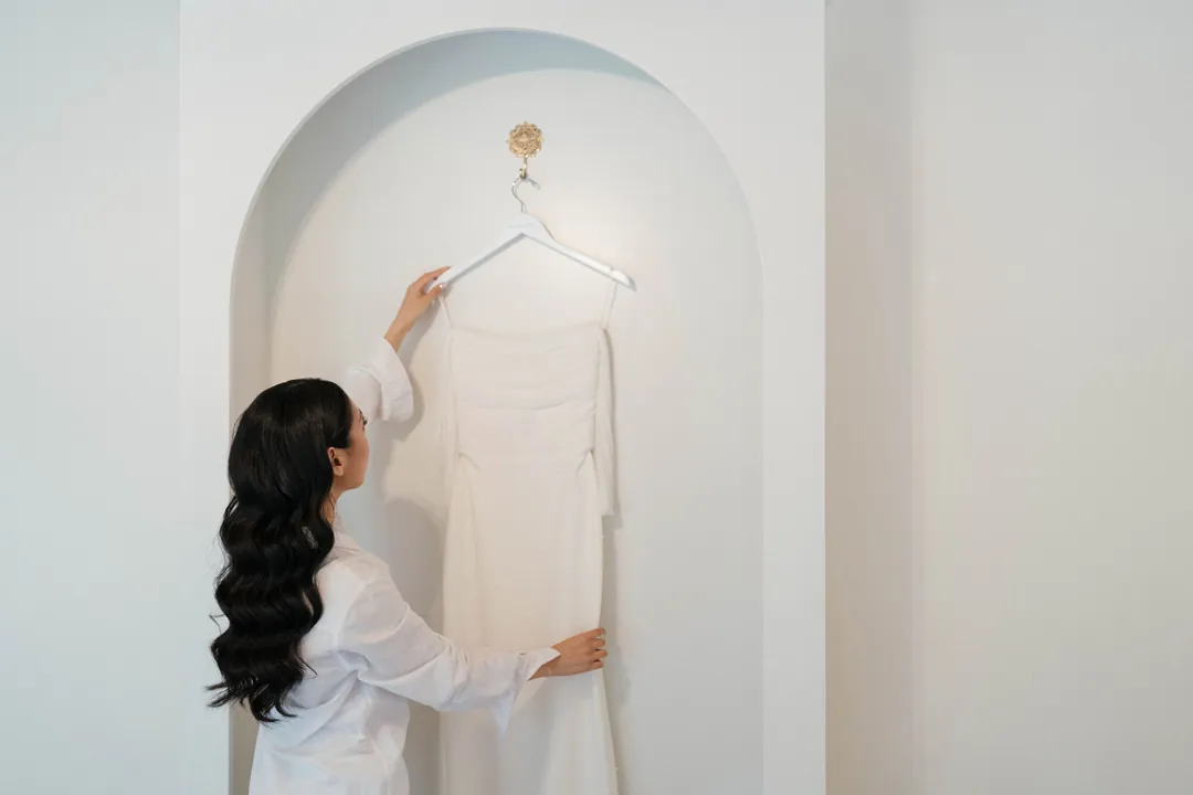 Bride reaching for her hanging wedding dress