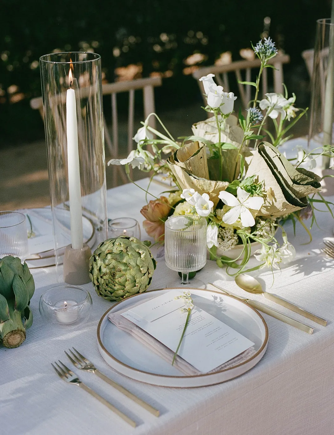 Pale floral centerpiece beside gold flatware and a green napkin