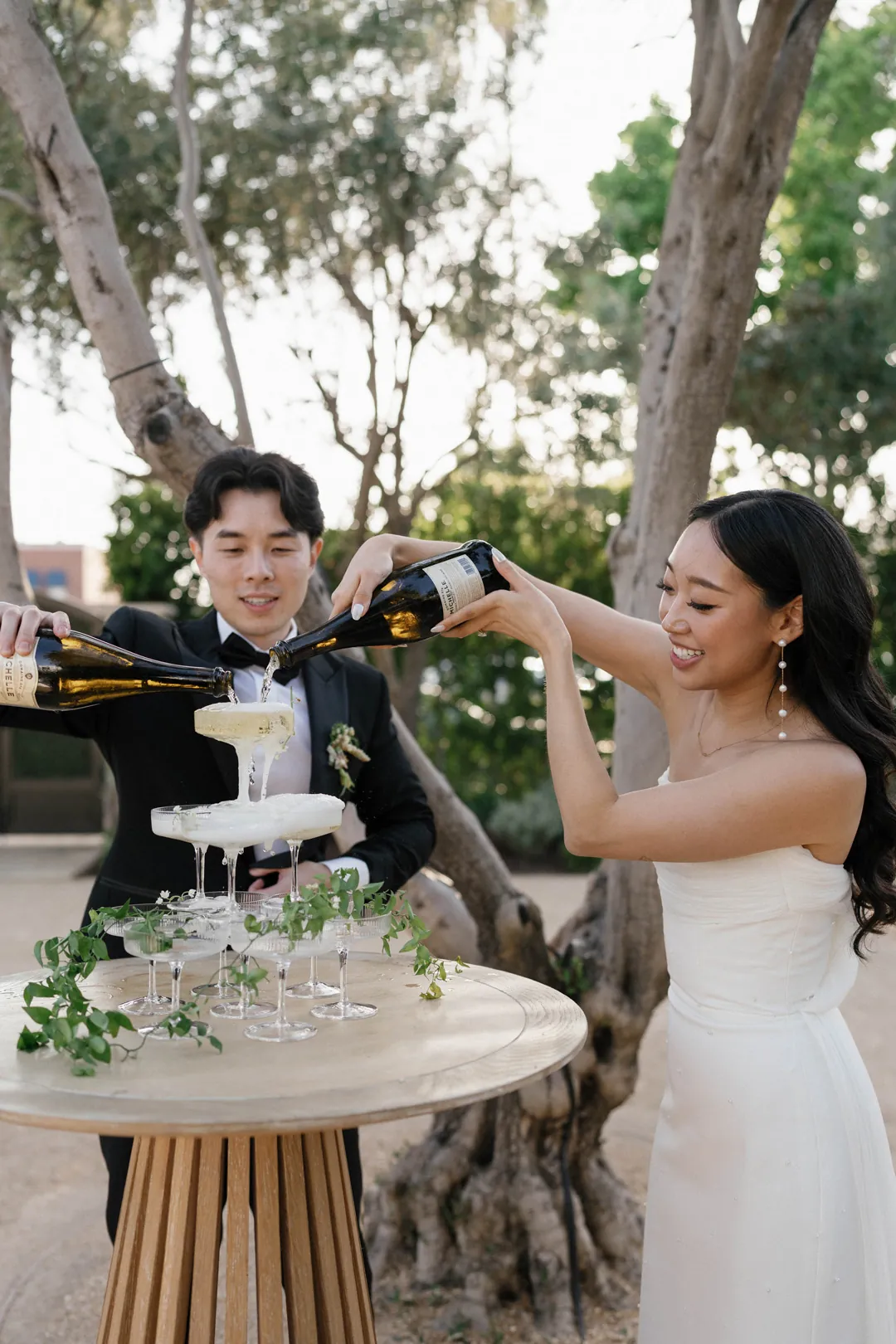 Bride and groom pouring drinks into stacked champagne glasses