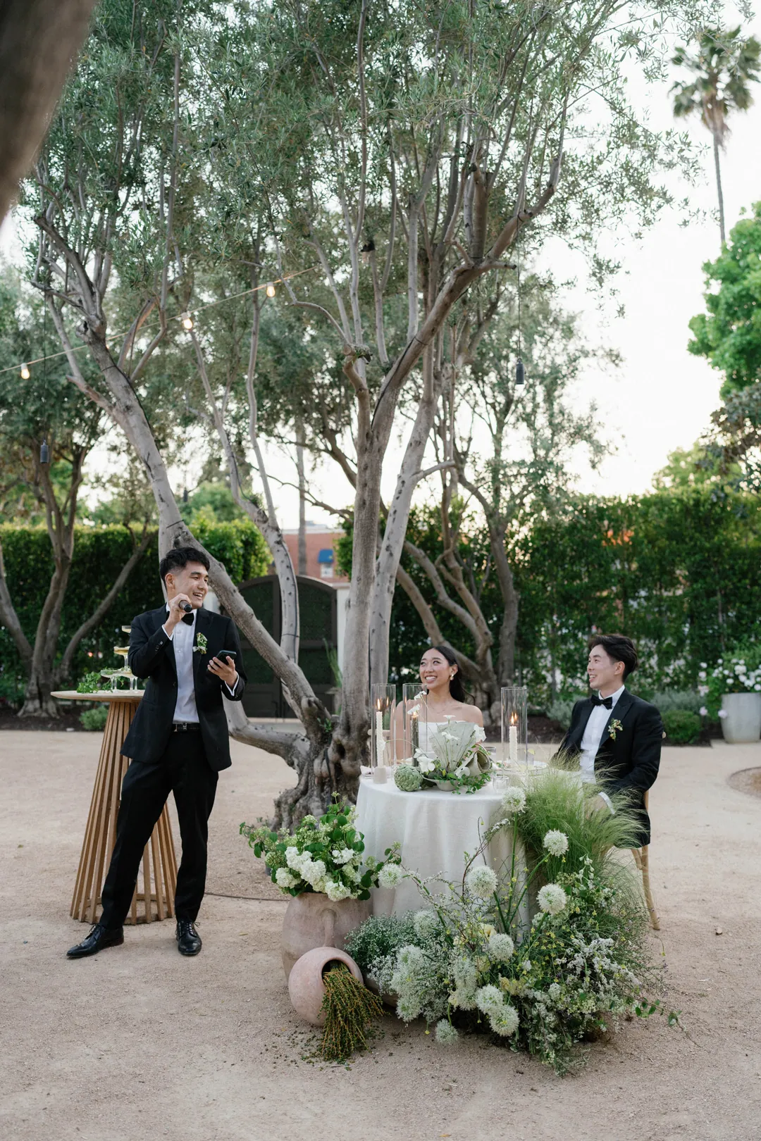Guest addressing the couple seated at an outdoor sweetheart table