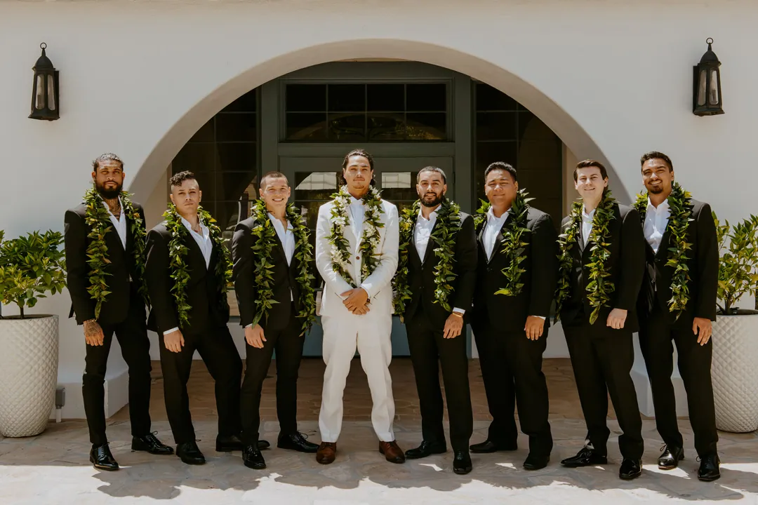 Groom and groomsmen wearing leis outside an arched entrance