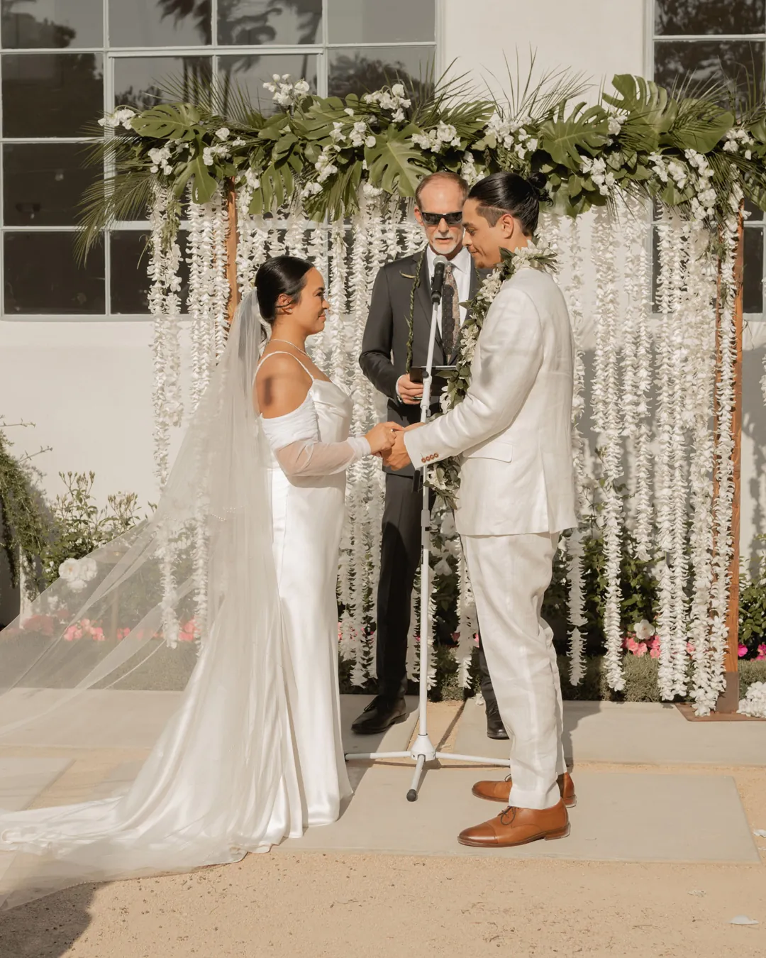 Bride and groom exchanging vows beneath hanging flowers