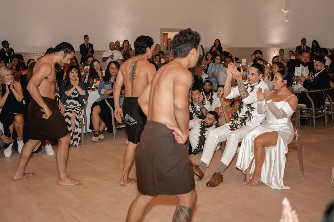 Performers dance in front of the seated couple and reception guests.