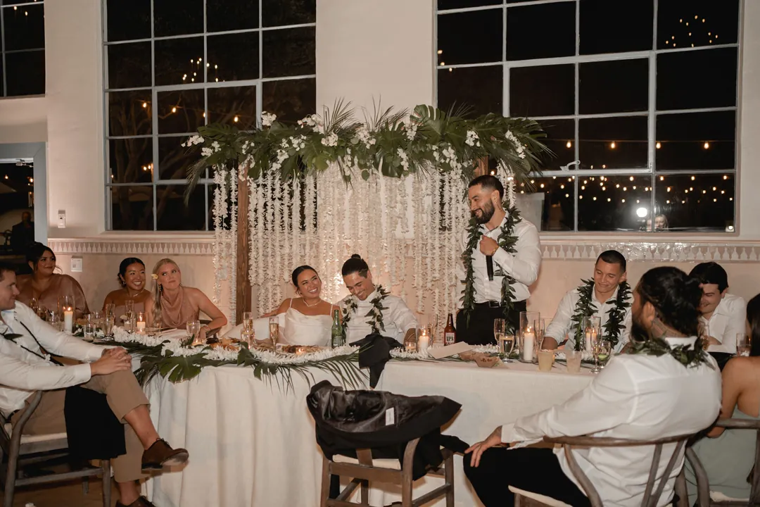 A guest gives a toast beside the couple’s flower-decorated head table.