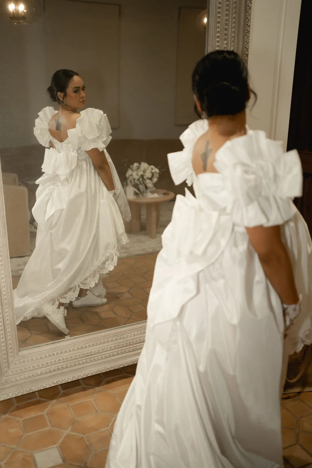 The bride looks at her reflection in a full-length dressing-room mirror.