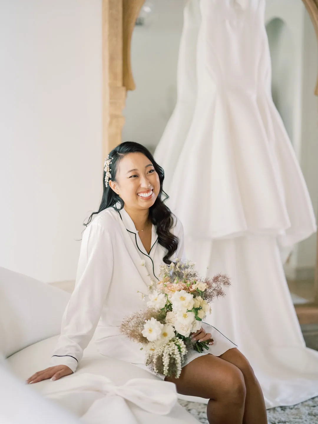 The bride holds a bouquet beside her hanging gown.