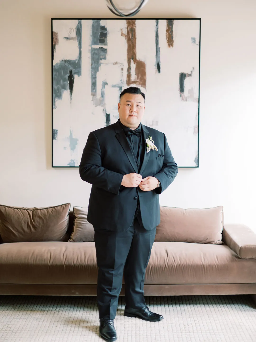 The groom poses in front of a lounge sofa.