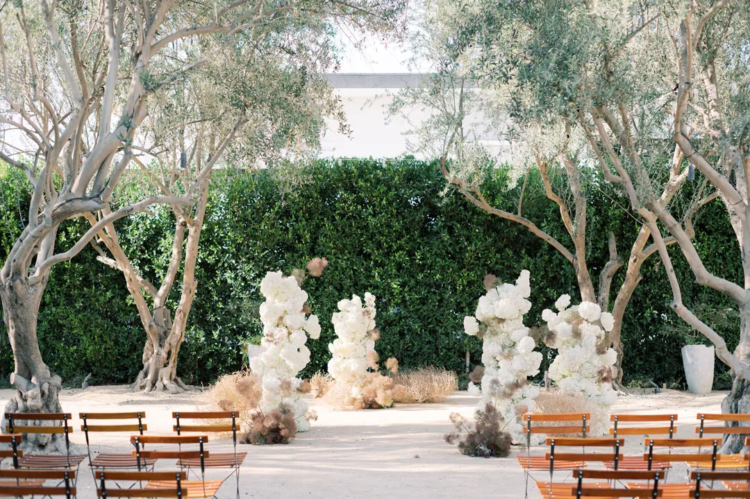 White floral columns frame the olive-grove ceremony backdrop.