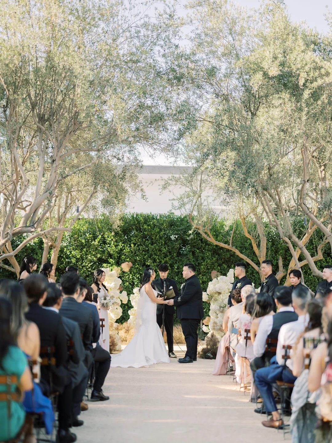 Outdoor ceremony viewed from the flower-lined center aisle