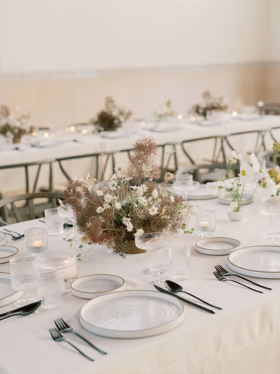 Pale floral centerpiece and white place settings on a reception table