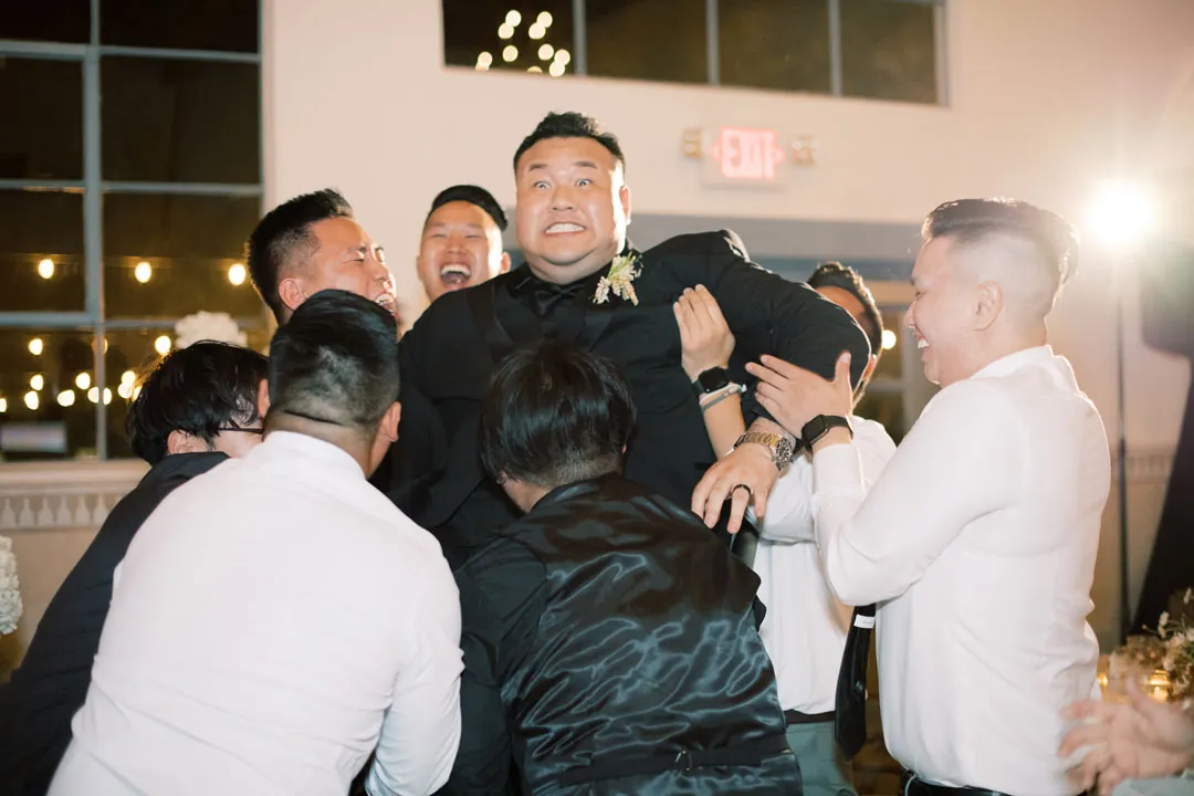 Guests lifting the groom during reception celebrations