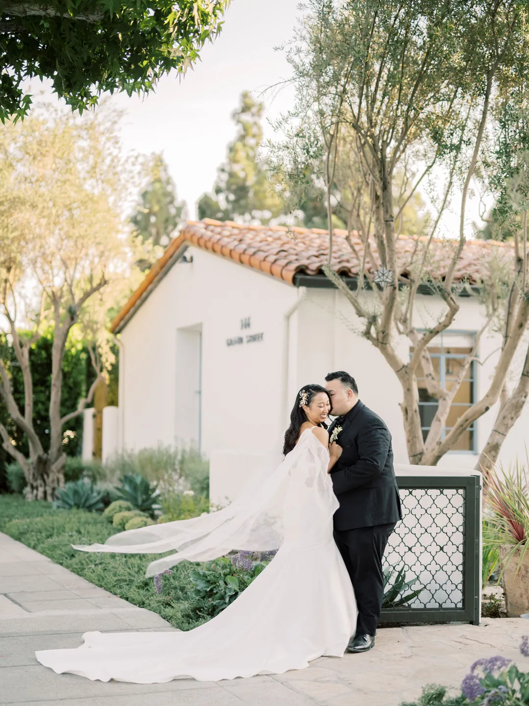 Groom kissing the bride beside the venue's white exterior