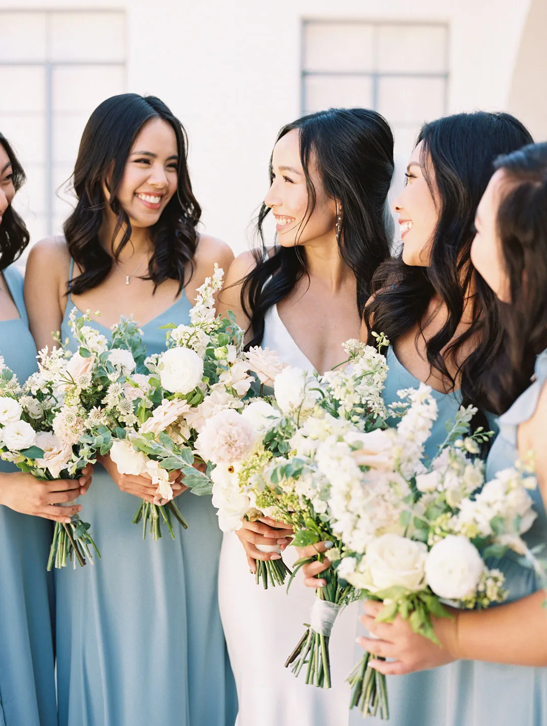 Bride and bridesmaids smiling with pale bouquets