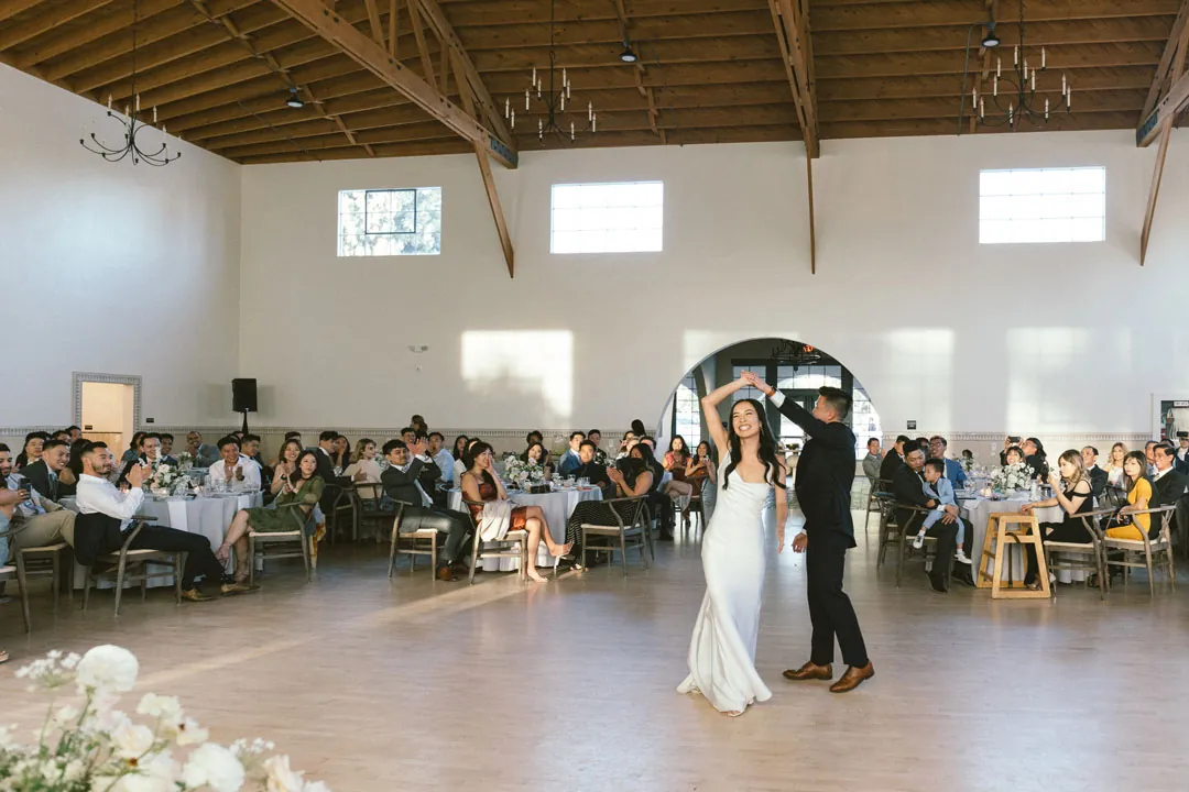 Newlyweds sharing their first dance as reception guests watch.