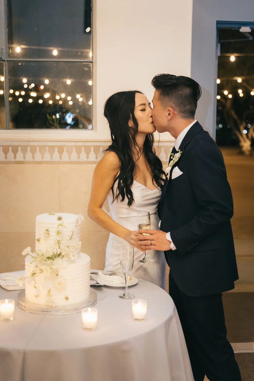 Newlyweds kissing beside their wedding cake.