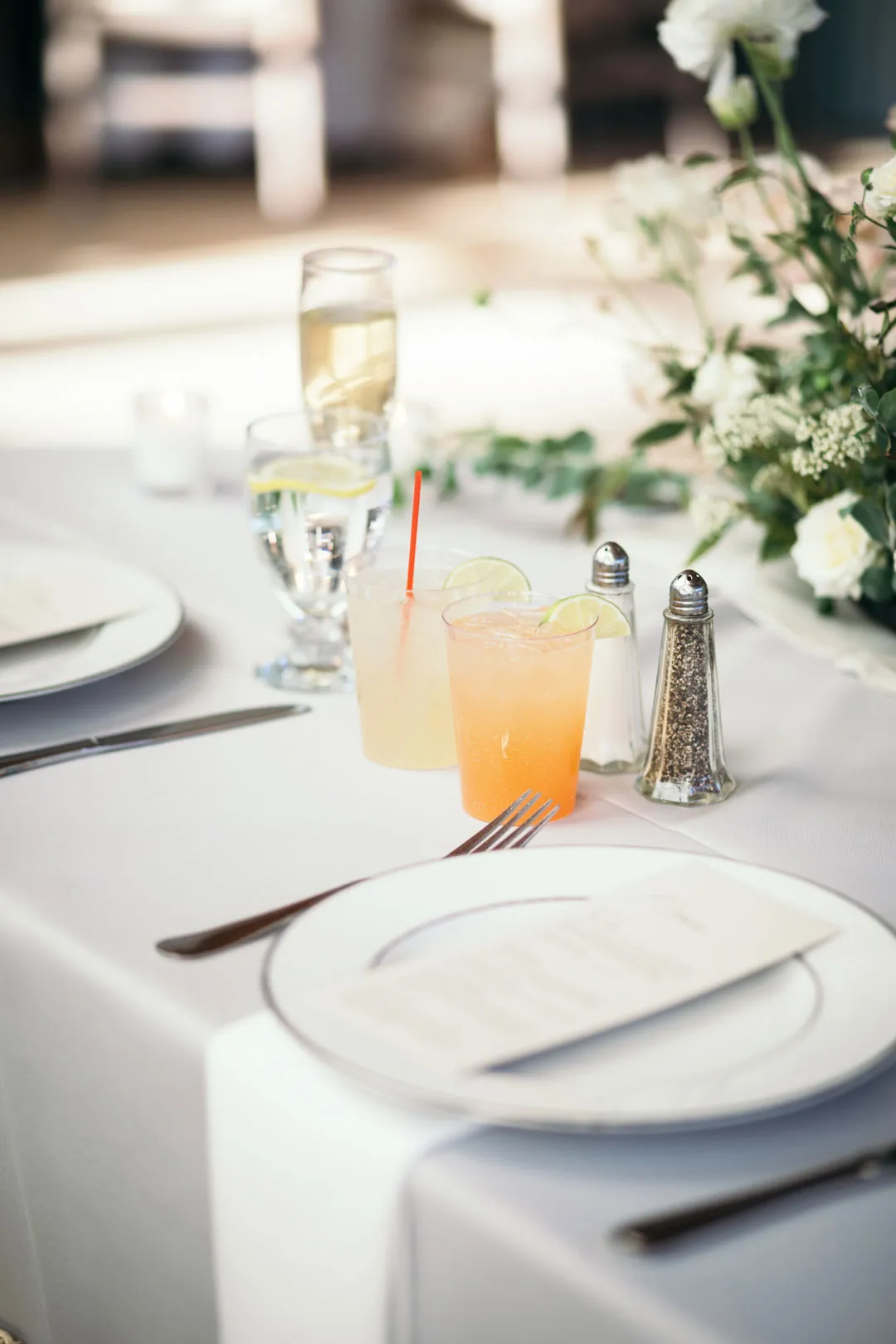 Reception place setting beside a pale drink and white flowers