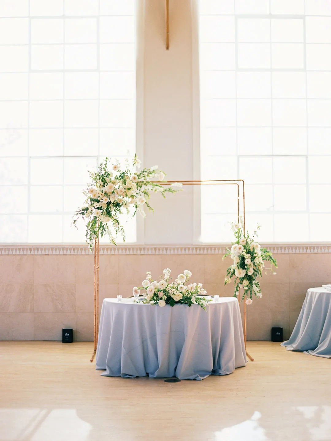 Sweetheart table with blue linen beneath a floral frame