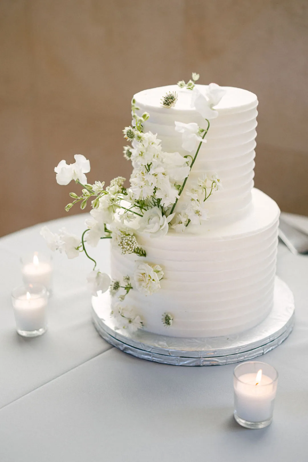 White two-tier wedding cake decorated with greenery and flowers.
